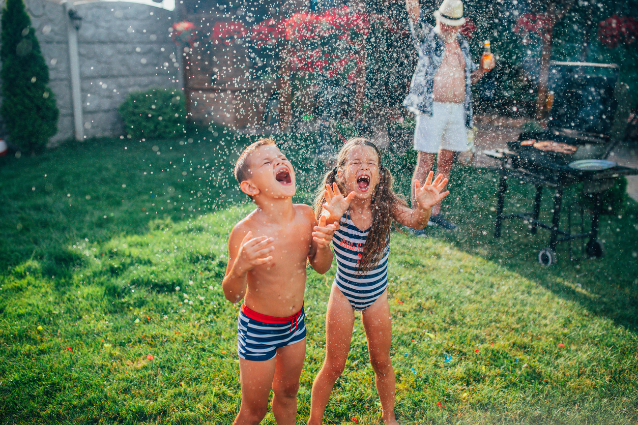 Kids playing in a sprinkler on a clean backyard lawn